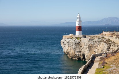 The red and white lighthouse of Gibraltar in sunshine in June. The Strait of Gibraltar and the mountains of the Spanish south coast can be seen in the background.