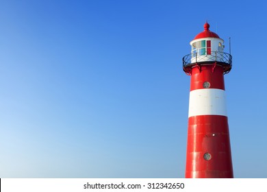 A red and white lighthouse at sea under a clear blue sky. Photographed near Westkapelle in Zeeland, The Netherlands. - Shutterstock ID 312342650