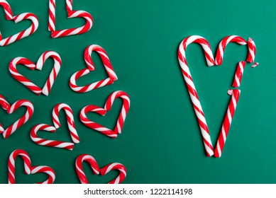 Red and white mini candy canes, arranged in heart shapes, and big candy canes in the shape of a broken heart, on a green background. - Powered by Shutterstock