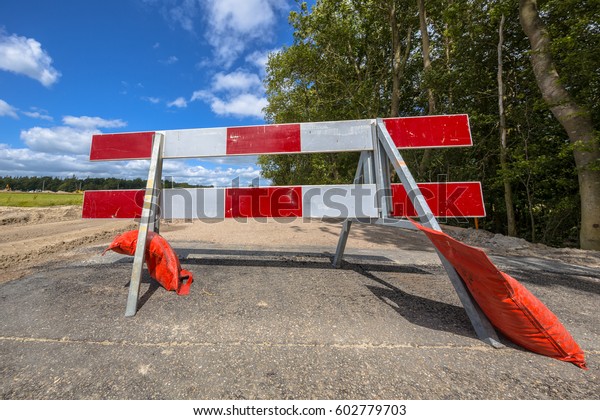 Red and white no entry roadblock on a
small asphalt country road and trees in
background