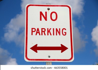 Red and White No Parking Sign with Double Bi-Directional Arrow Against Partly Cloudy Blue Sky