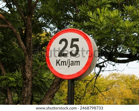 A red and white pole marking the maximum speed limit of 25 km per hour with a background of trees in a housing complex