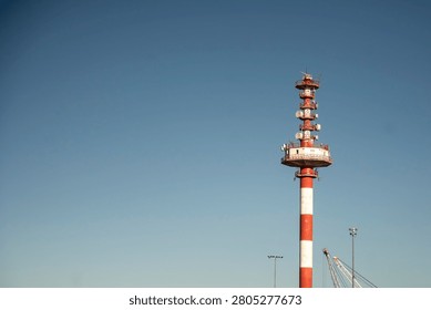 Red and white radar tower with multiple antennas against blue sky.