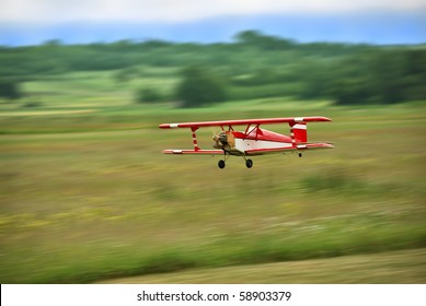 Red And White Radio Controlled Aircraft With Methanol Engine Flying Over Grassy Field. The Image Shows Motion Blur.