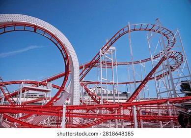 Red and white roller coaster loop at an amusement park under a clear blue sky with seagulls flying. Exciting summer attraction and fun concept for travel, family vacation, and thrill seekers.
