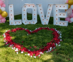 Red And White Rose Petals In The Shape Of A Heart With Letters Spelling Love Behind It On A Green Grass Lawn.