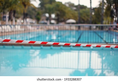 Red White Tape In Front Of Empty Hotel Resort Swimming Pool Closed During Evening Cleaning, Blurred Water Background