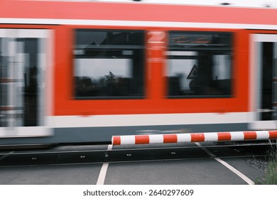 A red and white train is passing through a red and white barrier. The train is moving quickly and the barrier is in the way