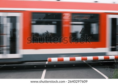 A red and white train is passing through a red and white barrier. The train is moving quickly and the barrier is in the way
