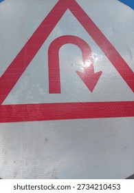 Red and white triangular warning sign with curved arrow symbol indicating direction change or turn ahead on road safety signage