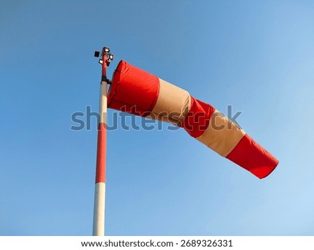A red and white windsock blowing in the wind against a clear blue sky. Aviation weather vane for direction
