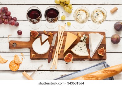 Red And White Wine Plus Different Kinds Of Cheeses (cheeseboard) On Rustic Wooden Table. French Food Tasting Party Or Feast Scenery From Above (top View).