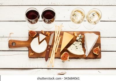 Red And White Wine Plus Different Kinds Of Cheeses (cheeseboard) On Rustic Wooden Table. French Food Tasting Party Or Feast Scenery From Above (top View).