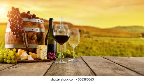 Red and white wine served on wooden planks with keg, vineyard on background, copyspace for text