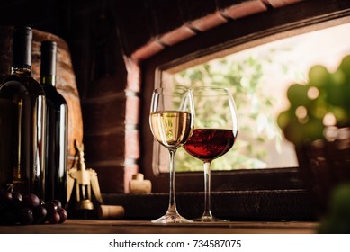 Red and white wine tasting in the winery: full wine glasses next to a window and lush vineyard on the background, winemaking concept
