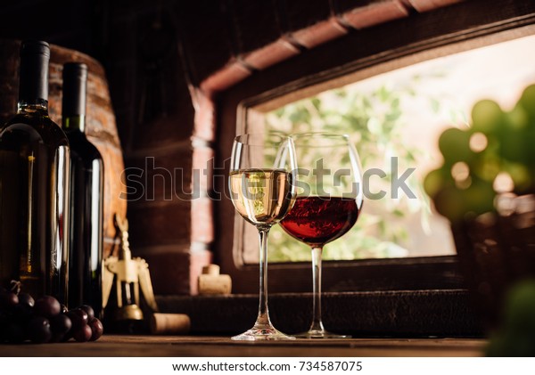 Red and white wine tasting in the winery: full\
wine glasses next to a window and lush vineyard on the background,\
winemaking concept