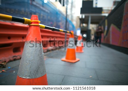 Red and white witches hat cone traffic warning signage barrier applying on busy street downtown on pedestrian footpath, road under construction in Sydney city CBD,  Australia 