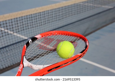 Red Wilson tennis bracket with Head Pro tennis ball and tennis court behind them. Closeup color image from high angle view. Photographed in sunny Dubai. Perfect summer sport!