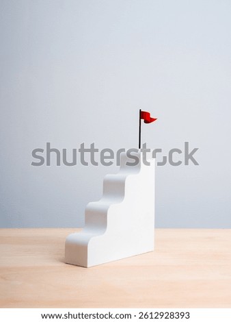 Red win flag on top of white staircase as bar graph chart steps on wood table, white vertical background. Business growth process, profit and investment, mission and success, leadership plan concepts.