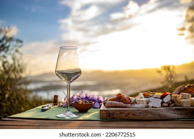 A red win glass and a cheese plate at beautiful sunset. An outdoor romantic picnis.