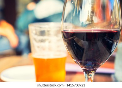 Red wine and beer glass on wooden table with blurry people background