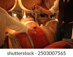 Red wine being poured from a wine thief in the barrel room of a winery.