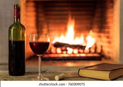 Red wine and a book on a wooden table, blur burning fireplace background