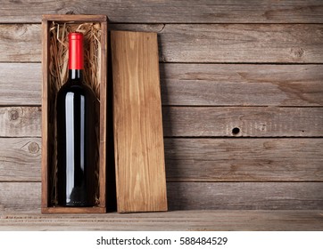 Red wine bottle in box in front of wooden wall. With copy space