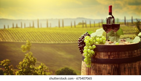 Red wine bottle and wine glass on wodden barrel. Beautiful Tuscany background