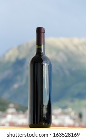 Red Wine Bottle With No Label On Outside In Front Of A Blurry Mountain And A Town