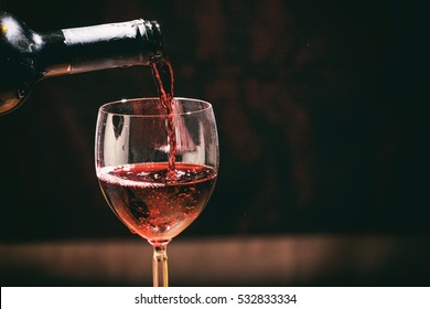 Red Wine Bottle Pouring Wine In A Glass On A Dark Bar Background, Copy Space