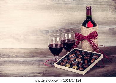 Red wine bottle,two glasses of wine, box of chocolates, rose with decoration by red heart on wooden table. Valentines day celebration concept. Copy space.