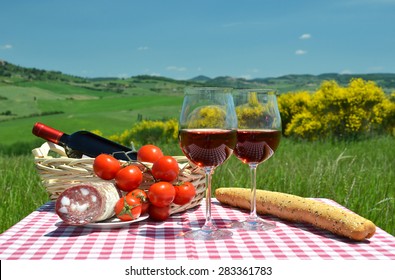 Red wine, bread and tomatoes on the chequered cloth against Tuscan landscape. Italy