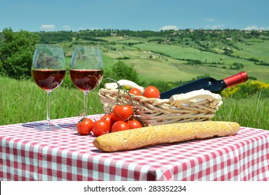 Red wine, bread and tomatos on the chequered cloth against Tuscan landscape. Italy