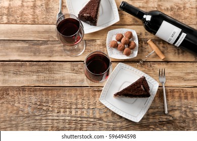 Red wine, chocolate truffles and tasty cake on wooden background