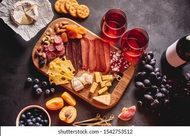 Red wine with different kinds of cheese, charcuterie assortment, crackers, grapes, nuts and berries on the dark concrete background - Powered by Shutterstock