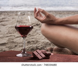 Red wine glass with chocolate and woman practicing yoga on the beach