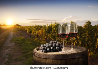 Red Wine Glass And Grape On Wooden Barrel With Vineyard Background