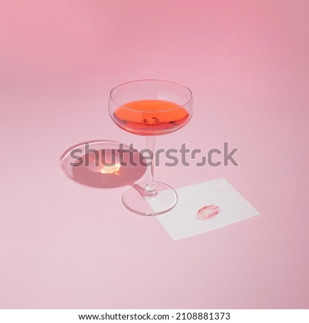 Red wine glass and romantic card with lipstick kiss on pastel pink background. Trendy and minimal Valentine's Day aesthetic.