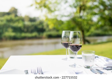 Red Wine On Table Set And  Green Grass Background In The Garden