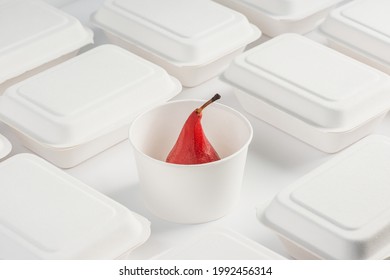 Red wine poached pear in a paper cup among white takeaway boxes. Minimalistic photo of gourmet dessert for delivery.