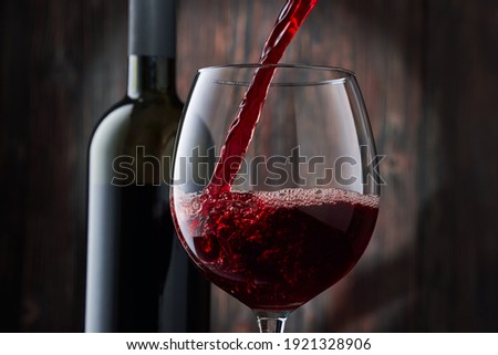 Red wine is poured into a glass from a bottle on a blurred wooden background, a stream of red wine from the bottle swirls in the glass, close-up. Free space for text.