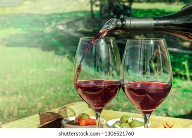 Red Wine Poured Into Glasses Outside, With Blurred Greenery In The Background For Copy Space