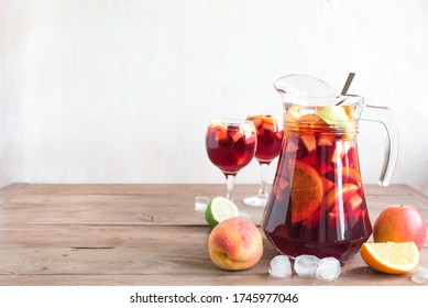 Red Wine Sangria in pitcher and glasses on wooden table, copy space. Homemade refreshing drink - fruit sangria or punch with ice.