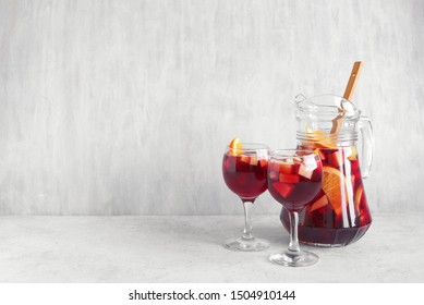 Red wine sangria or punch with fruits and ice in glasses and pitcher. Homemade refreshing fruit sangria on white background, copy space.