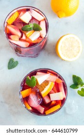 Red wine sangria or punch with fruits, mint and ice in glasses. Homemade refreshing fruit sangria over rustic white table, copy space