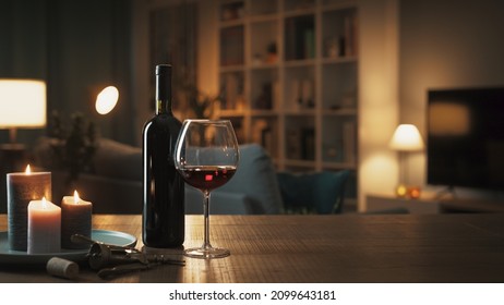 Red wine tasting at home: wine bottle, wineglass, corkscrew and candles on a table in the living room at night - Shutterstock ID 2099643181