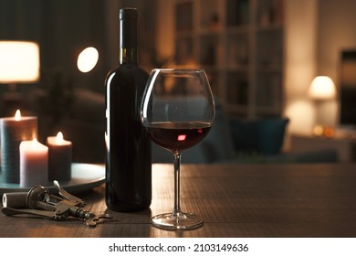 Red Wine Tasting At Home: Wine Bottle, Wineglass, Corkscrew And Candles On A Table In The Living Room At Night