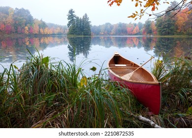 Red Wood Canoe On Shore Of A Small Lake With An Island On A Cloudy Autumn Morning