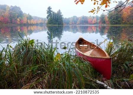 Red wood canoe on shore of a small lake with an island on a cloudy autumn morning